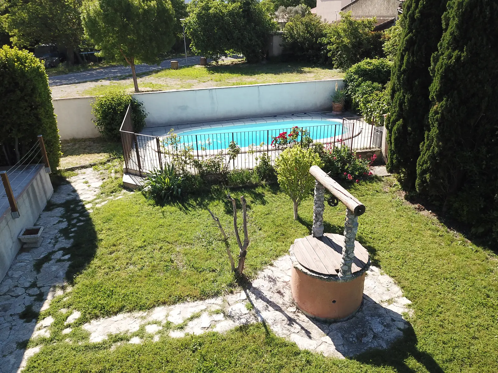 Der alte Brunnen auf dem Rasen, vor dem umzäunten Pool